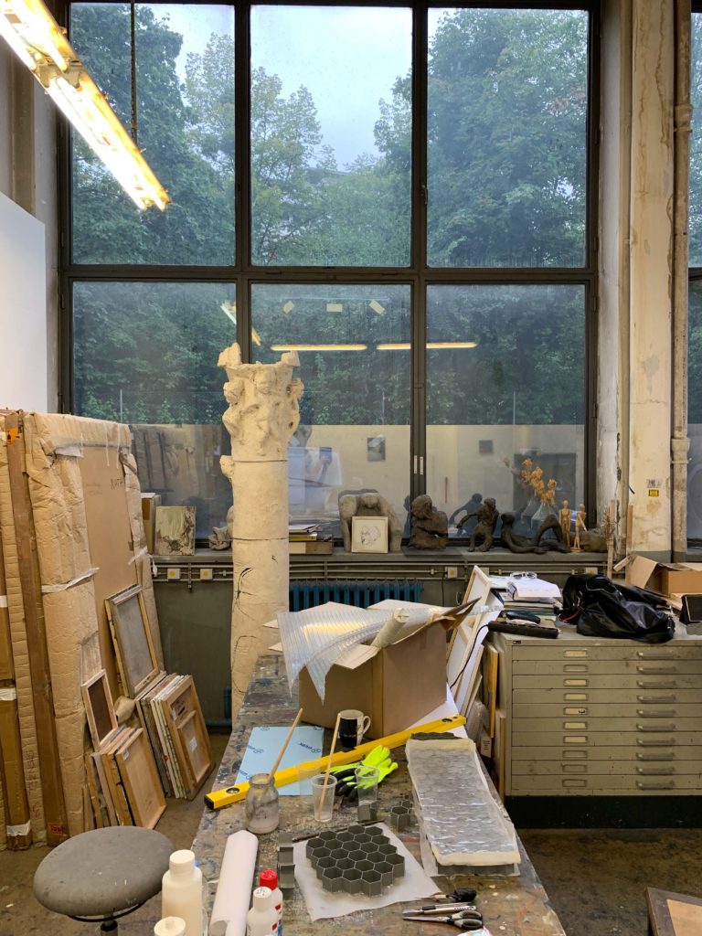 Snapshot of the studio showing artworks laying against the wall, several materials on the work table and a large window in the background.