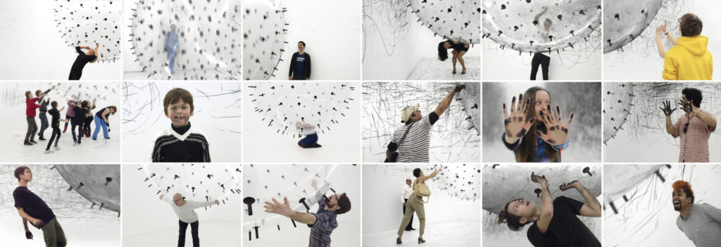 Collage of several snapshots of visitors interacting with a sphere covered in charcoal sticks, leaving marks on the gallery’s white walls at the interactive installation ADA