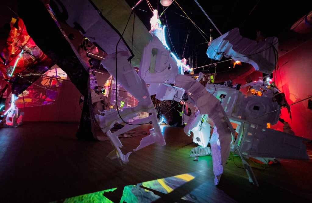 Large room installation with salvage styrofoam, billboards, neon, painted photographs and projected video