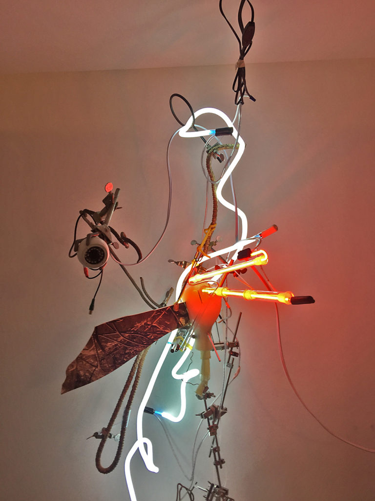 Hanging sculpture with rebar, neon, and a security camera